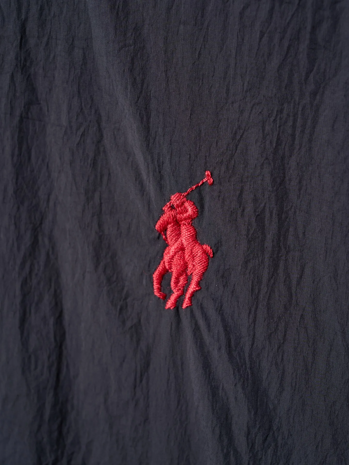P640 Actual auction] Ralph Lauren/Ralph Lauren Pony Red Label lightweight cotton lapel coach jacket [Ready stock] S M L XL Material: high-density nylon taffeta Features: Density is about 210T-300T, smooth and slightly matte surface, excellent windproof and waterproof performance (with DWR water-repellent treatment), strong wrinkle resistance and easy care, in line with the positioning of American casual "durable and practical".  Color: Classic dark black, using vat dyeing process (dye penetrates into the fiber), the color fastness reaches ISO level 4 or above to avoid fading or color transfer after washing.  2. Lining fabric Material: Lightweight cotton-polyester blended lining (65% Polyester + 35% Cotton) Function: Reduce friction between the fabric and inner clothing, improve wearing smoothness; blended material has both breathability and durability to avoid the stuffy feeling of pure nylon lining.  Version and cutting process Version: Classic Coach Jacket, loose version, slightly dropped shoulder line (shoulder width is 1-2cm wider than the standard version), length to the hips, and slightly tapered straight sleeves, taking into account both freedom of movement and casual style. Embroidery technology: Polo horse logo on the left chest: flat satin stitch embroidery (satin embroidery), embroidery thread: 100% polyester high color fastness embroidery thread (the color number is consistent with the brand’s standard red color card), stitch density 12-15 stitches/cm, the outline of the horse logo is clear, and the details of the rider and horse are burr-free.  Embroidery positioning: precise positioning through the template (12cm from the neckline and 8cm from the placket) to ensure left and right symmetry and centering.  Topstitching technology: The seams of the body are made of double-needle flat seams (needle pitch 3cm/10 needles), the stitches are smooth and straight, the stitching color is dark black (the same color as the fabric), and the stitch width is 0.5cm, which enhances firmness while forming simple decorative lines.  1. Main body splicing, splicing of the front placket and body: The placket is made of double-layer folding + flat seam splicing, with a thickness of about 0.3cm to ensure that the buttons are not easily deformed when fixed; the edges of the placket are cut with a hot knife to avoid burrs.  Sleeve panels are spliced ​​to the body: the armholes are spliced ​​with round-head keyhole machine seams + flat seams. After splicing, the armholes have a natural curvature and no sense of tightness during movement; the height of the sleeves is about 8-10cm, which is in line with the loose characteristics of casual jackets.  Main button: black urea resin button, matte surface treatment, buttonholes are hand-made keyholes (6 strands of cotton thread, keyhole density 8 stitches/mm), the edges of the eyelets are smooth and without burrs.  Collar buttons: The first button on the collar is a hidden button (diameter 12mm), which prevents the collar from opening and improves the neatness of wearing.